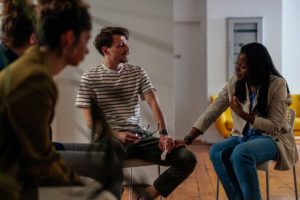 a photo of a group of people and one of women in the group touches a mans leg consoling him and telling him about interventions for addiction