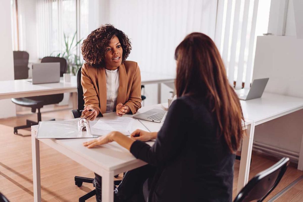 A woman is a personal finance coaches office and speaks with her during the womans personal financial coaching session