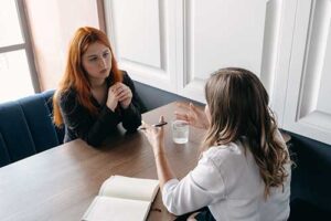 a patient sits with a therapist at a table going through how therapeutic recovery coaching can benefit the patient