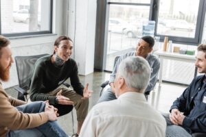 a group of people sit together in a circle while talking through issues in an addiction recovery coaching program