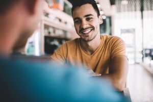 man sits with another person at a table in a coffee shop and talks about some tips to get through recovery