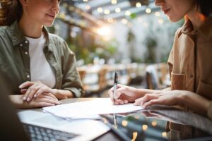 two people sit at table together outside one person takes notes about how financial coaching during recovery can help the other person