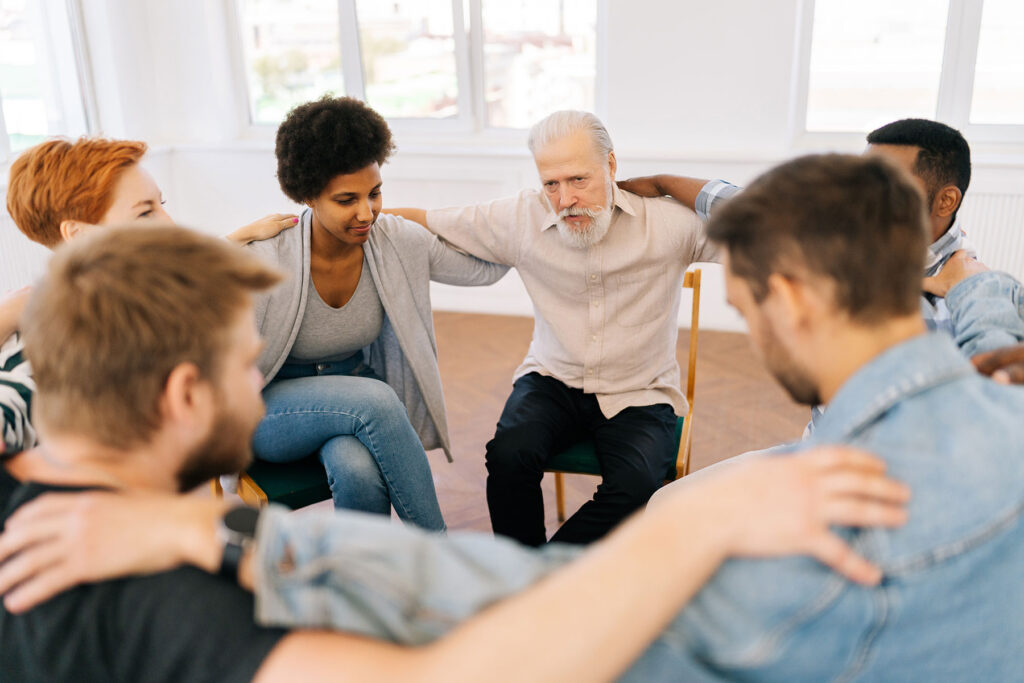 group of people sit and hug each other showing support to each other and one of the benefits of sober living homes