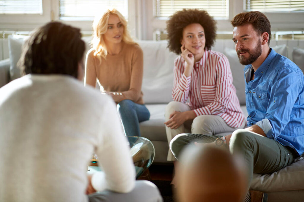 a group of people sit on a couch together and listen to someone talk about the sober living house rules