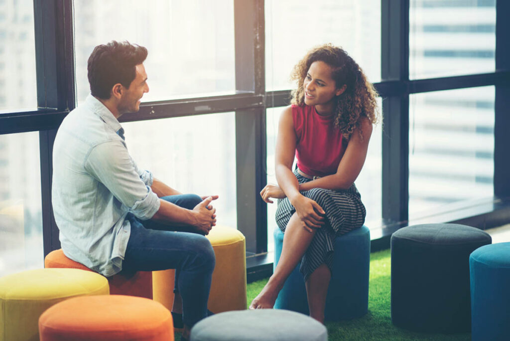 a woman and a man sit and talk to each other about how a recovery coaching treatment program can be beneficial to addiction recovery